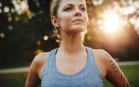 Close up portrait of fit young woman in sportswear standing outdoors and looking away. Confident fitness model in park.